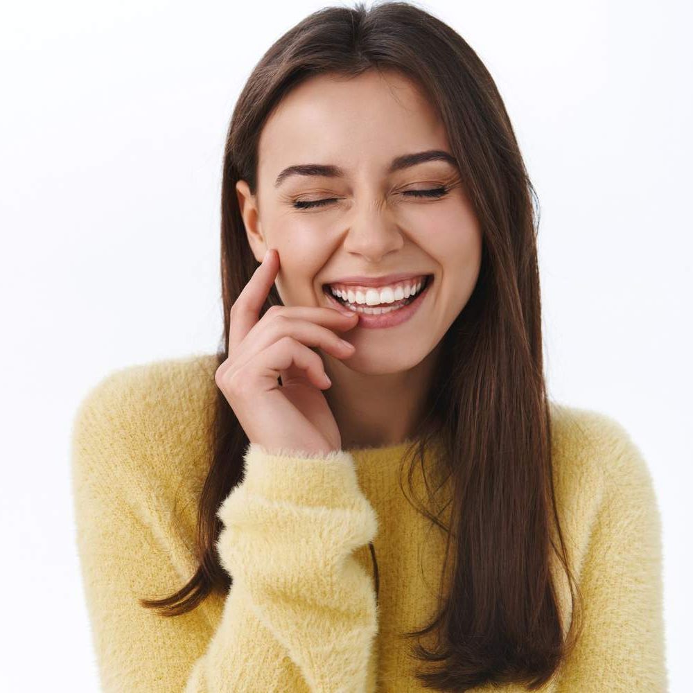 mujer-bonita-despreocupada-riendo-tontamente-ojos-cerrados-verdadera-sonrisa-toca-suavemente-mejilla-mientras-divierte-rie-tontamente-sobre-broma-hilarante-pared